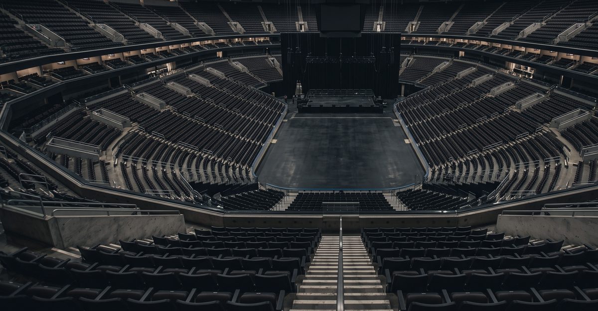 An empty arena seen from the upper tier, rows of seats facing a bare stage floor, illustrating where the earnings in Korean entertainment stocks actually come from, from korea-stock-guide.com
