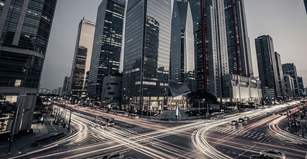Light trails from traffic crossing a city intersection at night between glass towers, illustrating the bull case for Korean equities after MSCI declined reclassification, from korea-stock-guide.com