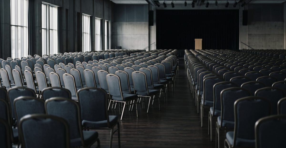 Rows of empty chairs facing an unlit stage in a large conference hall, illustrating the three-week investor programme Korea has scheduled for overseas institutions, from korea-stock-guide.com